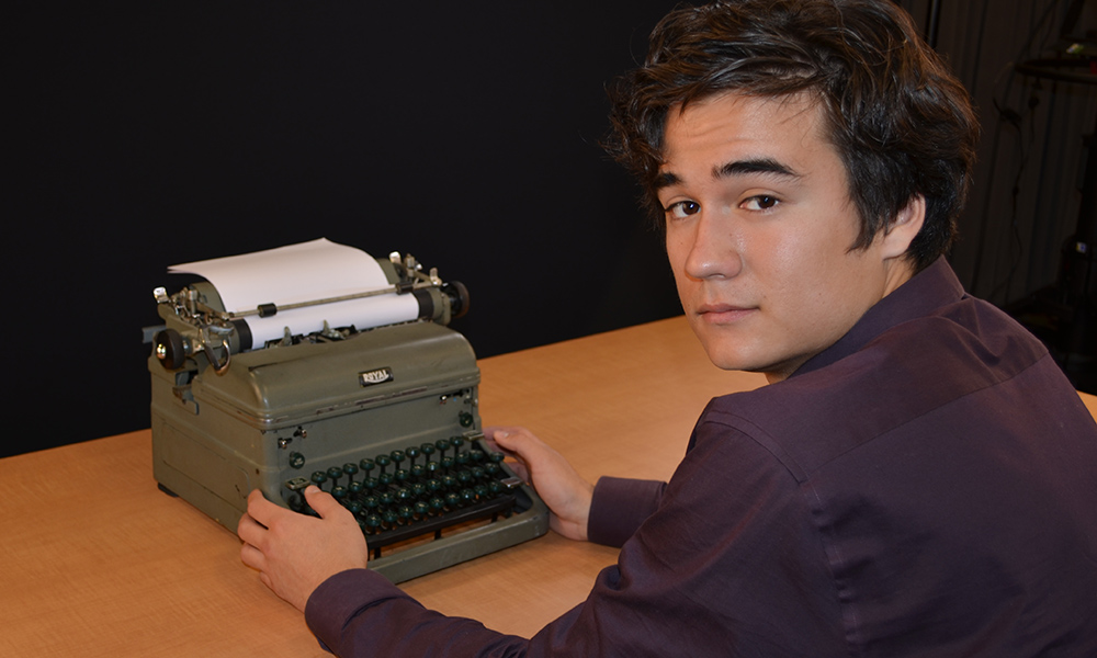 man-wearing-striped-jacket-and-pen-behind-ear-typing-on-typewriter-in